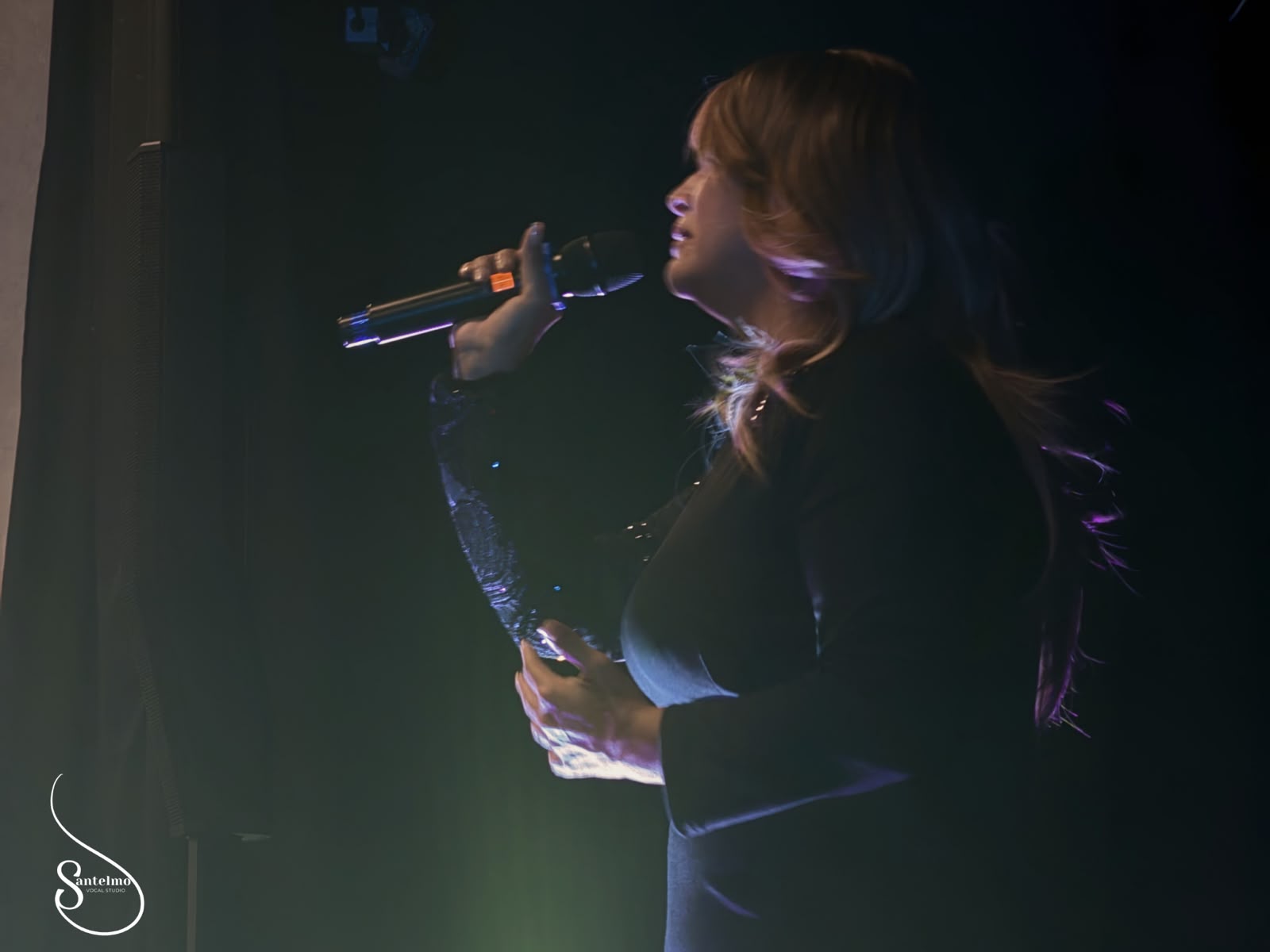 Alumna cantando con micrófono bajo luces de escenario